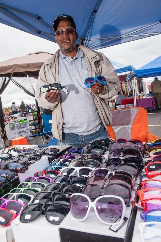 A man is standing in front of a table full of sunglasses.