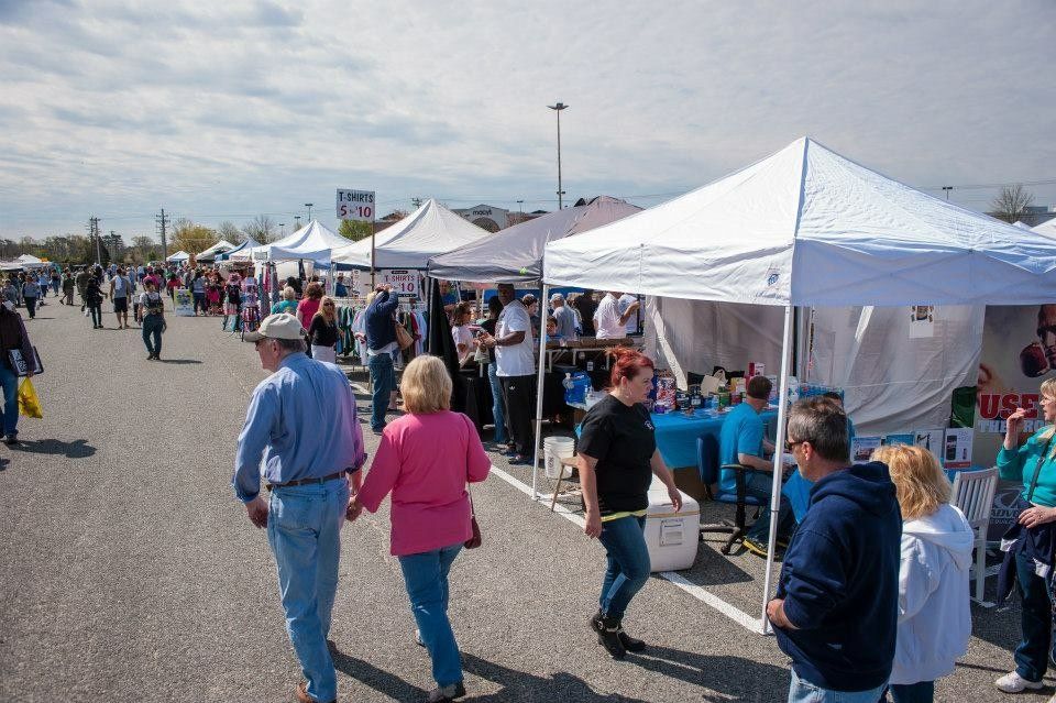 A group of people are walking through a parking lot filled with tents.