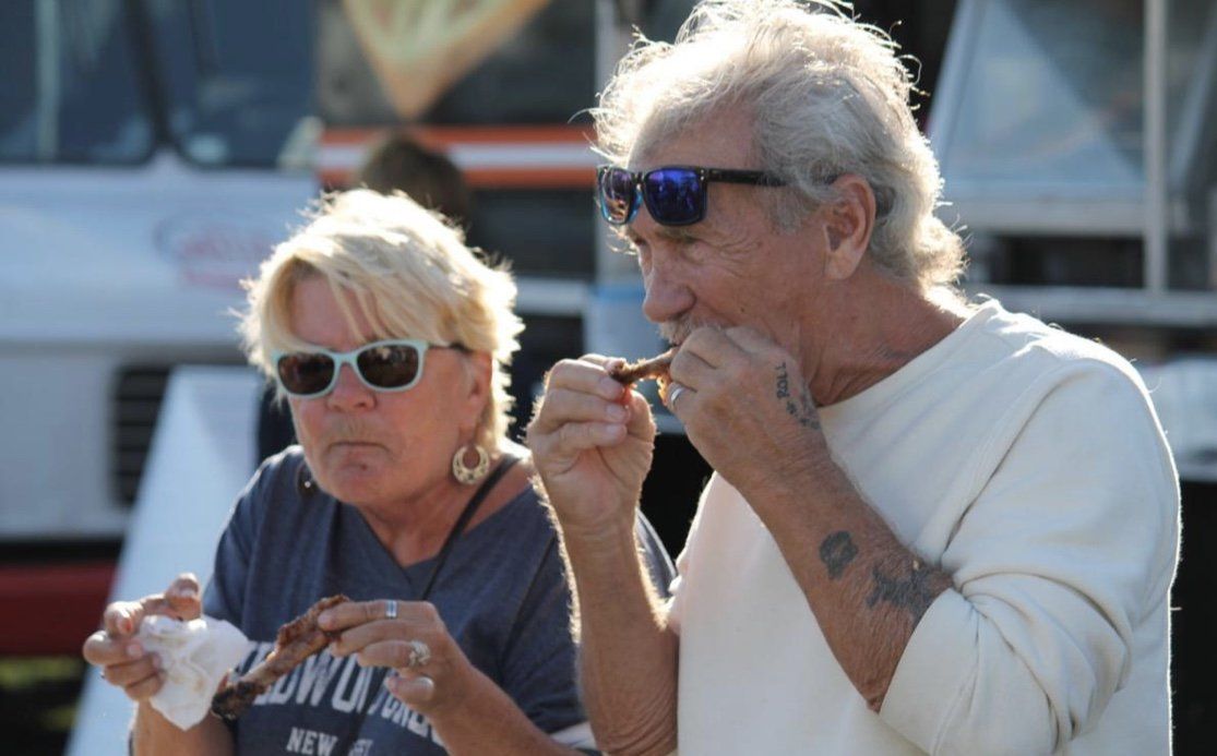 A man and a woman are eating food in front of a food truck.