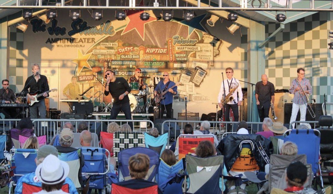 A group of people are sitting in chairs watching a band on a stage.