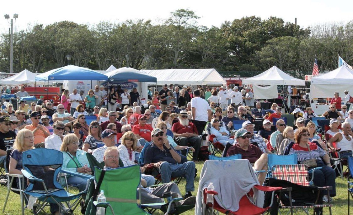 A large group of people are sitting in chairs in a field.