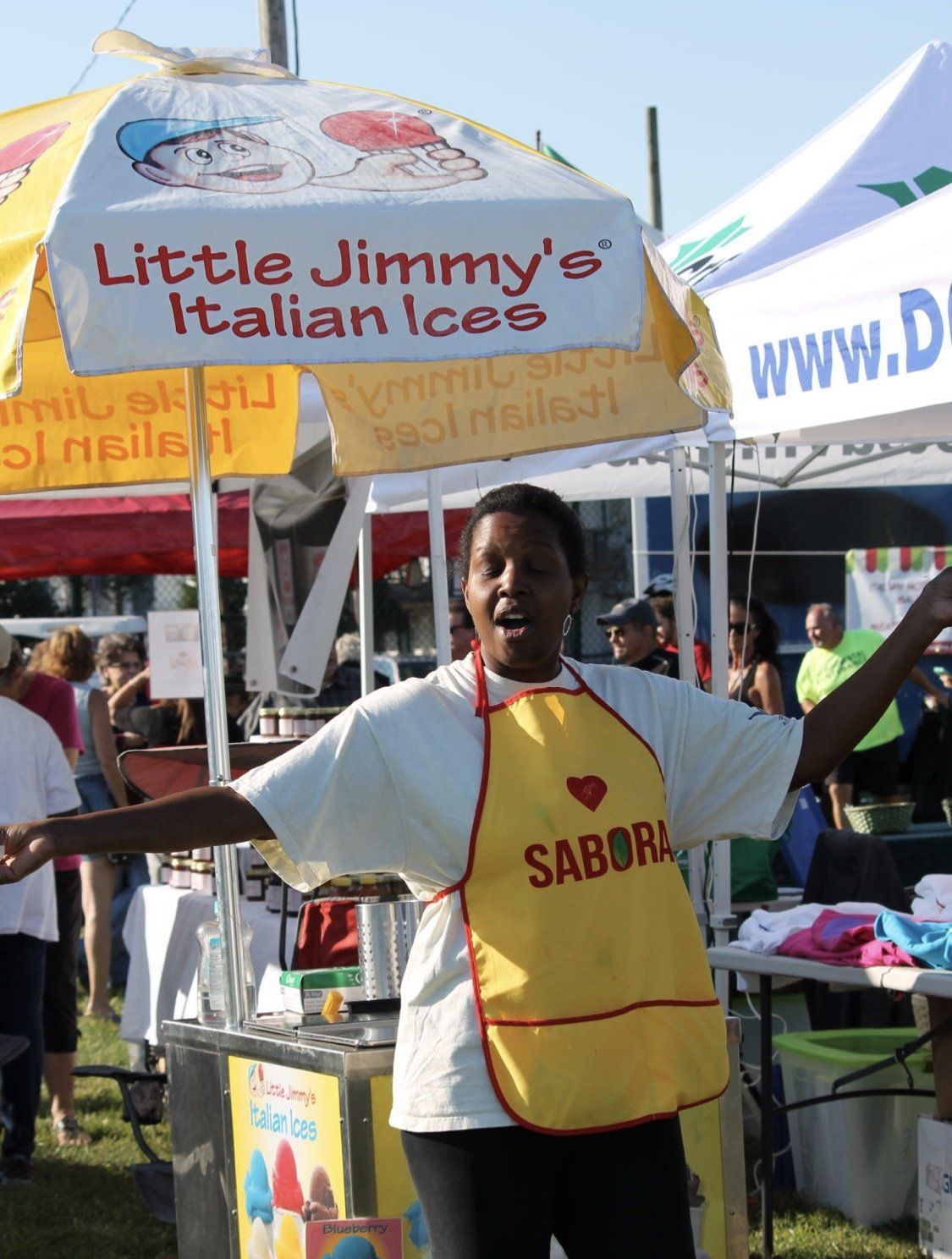 A woman stands in front of a little jimmy 's italian ice stand