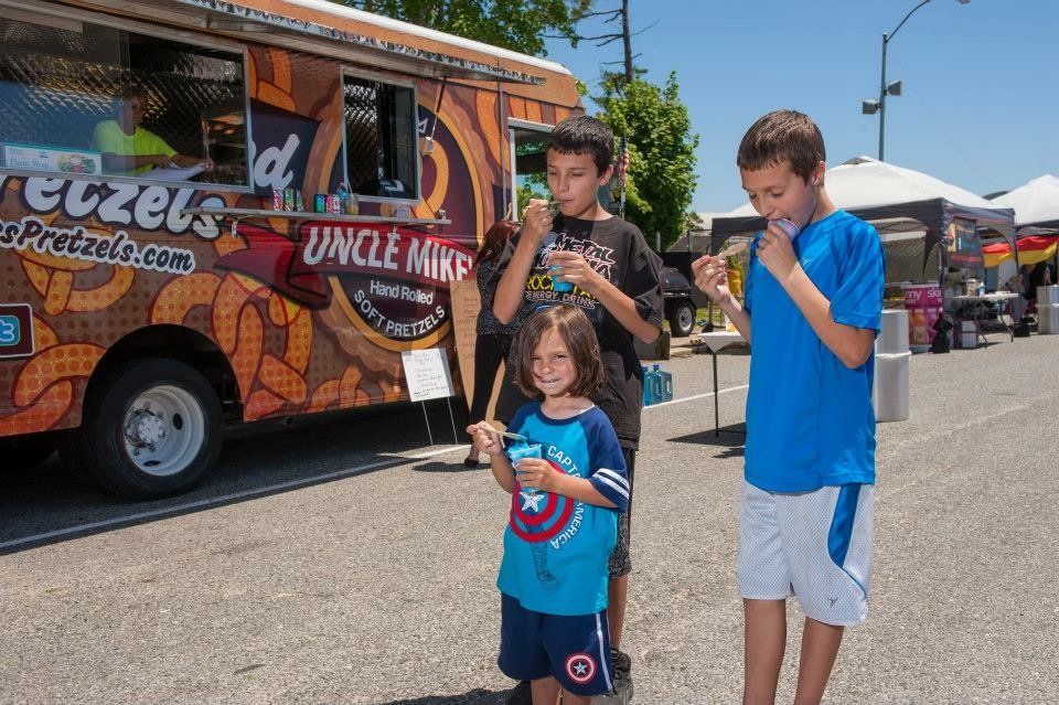 Three children are standing in front of a food truck that says uncle mike 's pretzels