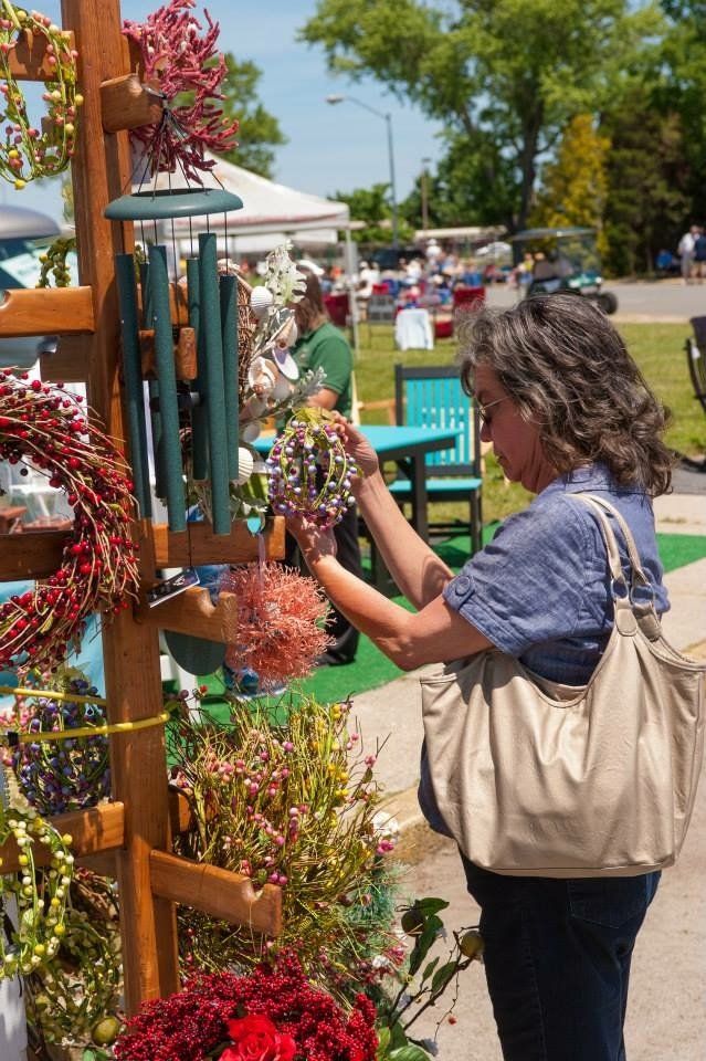 A woman is standing in front of a display of flowers and wind chimes.