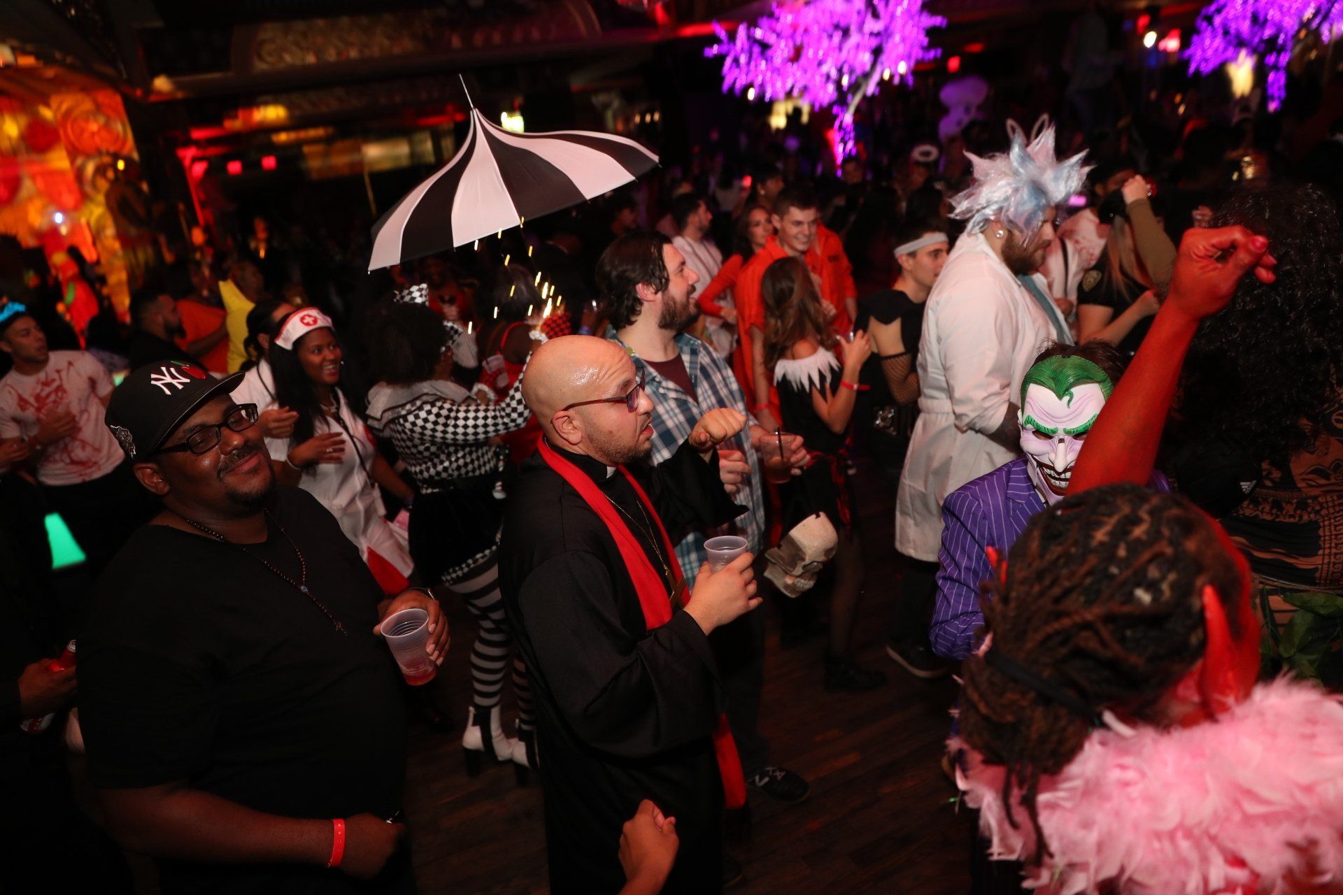 A crowd of people are gathered in a dark room at a halloween party.
