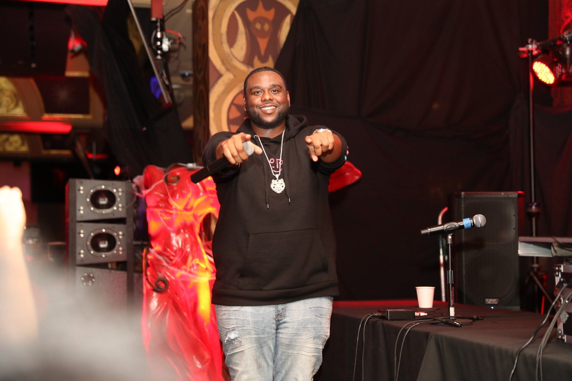 A man in a black hoodie is pointing at the camera