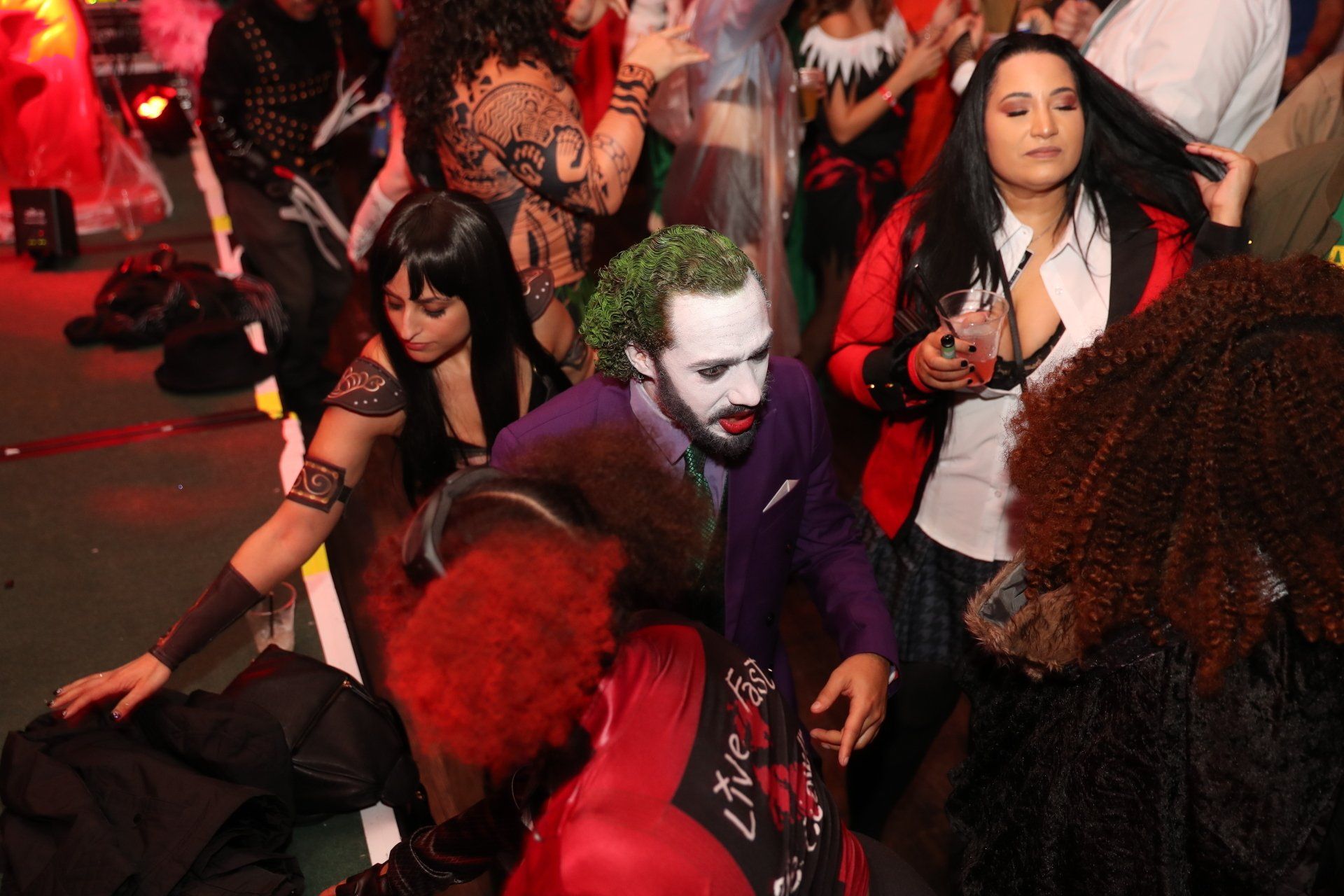 A man in a joker costume is standing in a crowd of people.