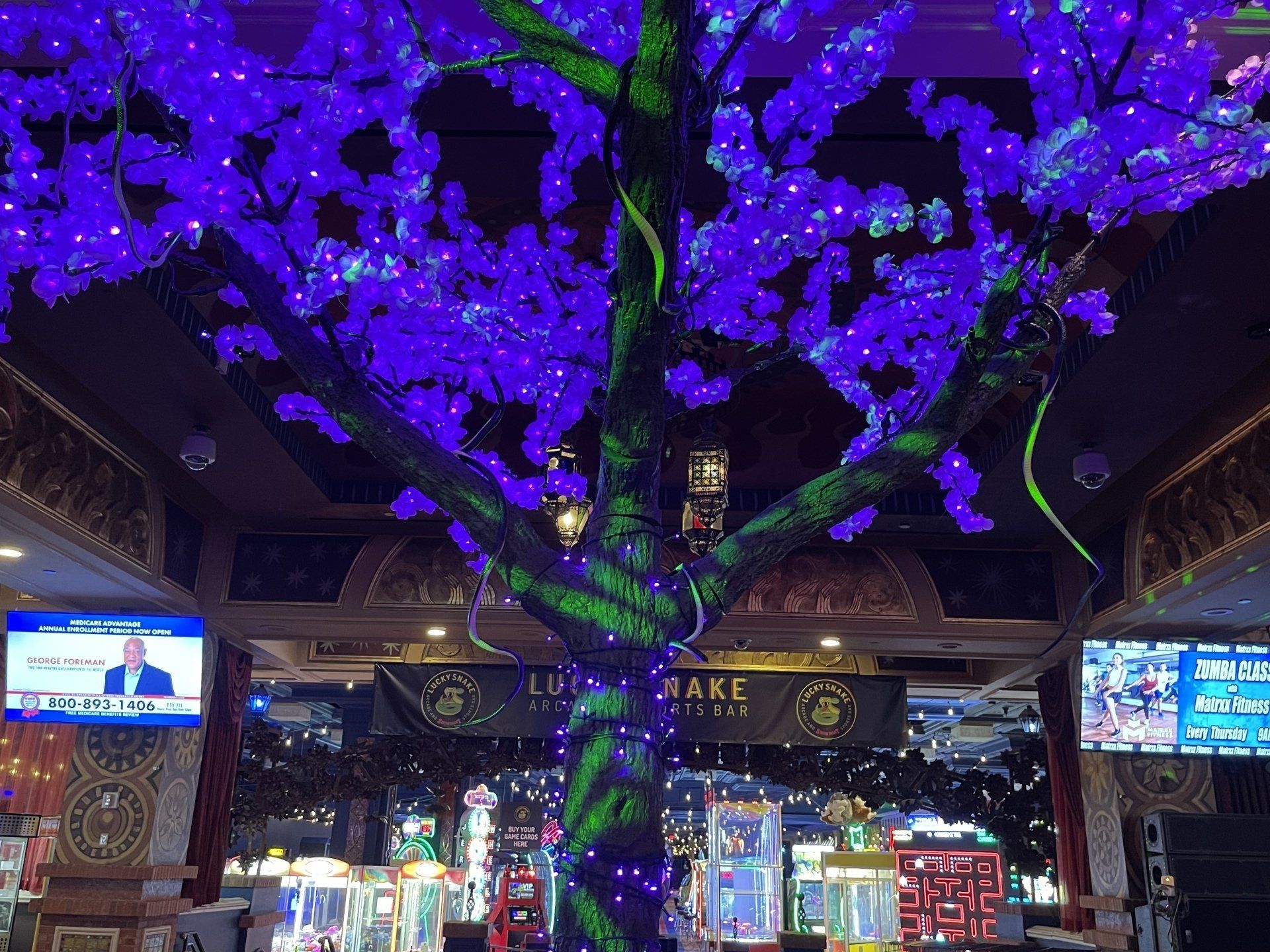 A large tree is lit up with purple lights in a casino.