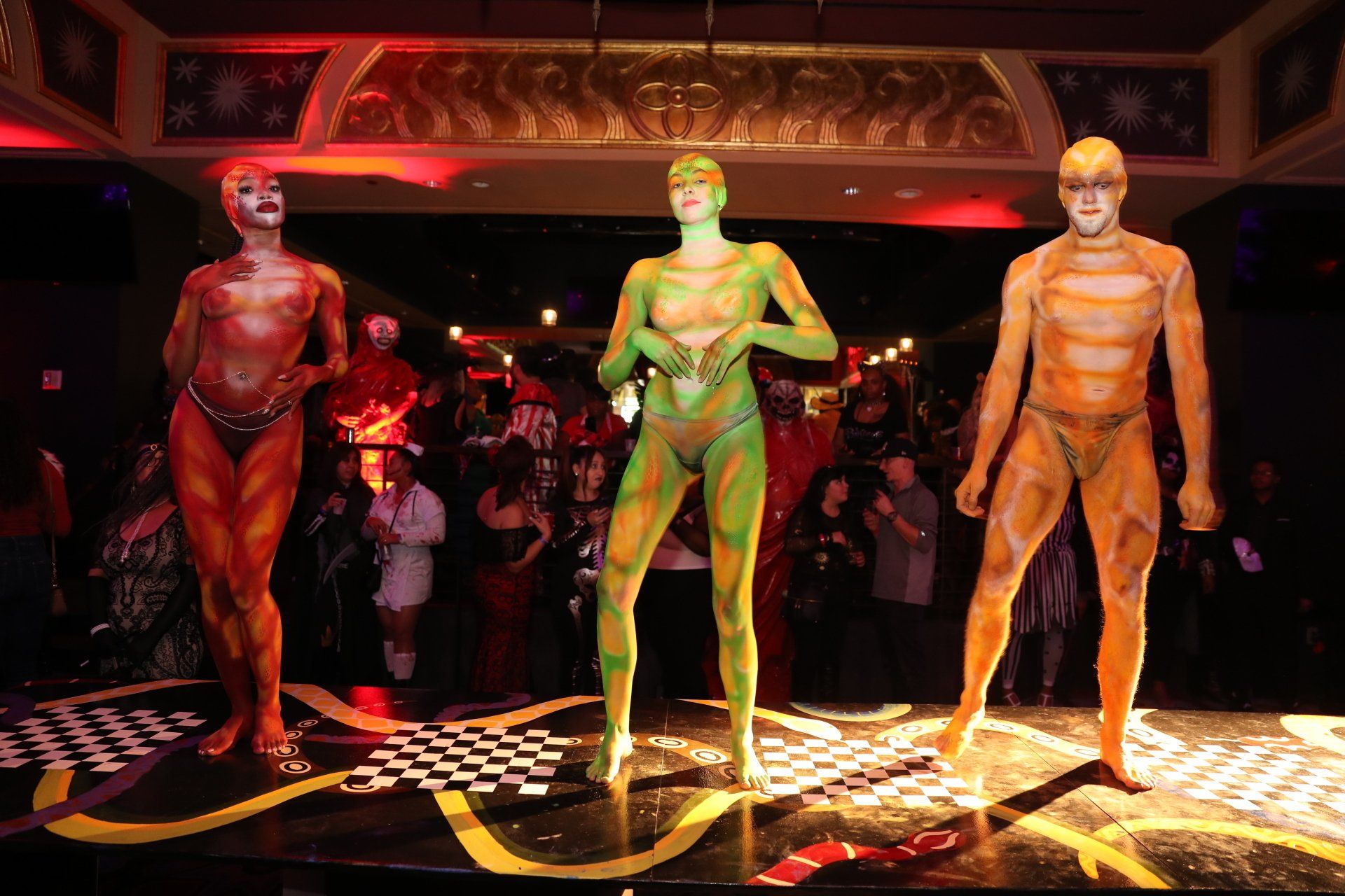 Three people painted in different colors are standing on a stage