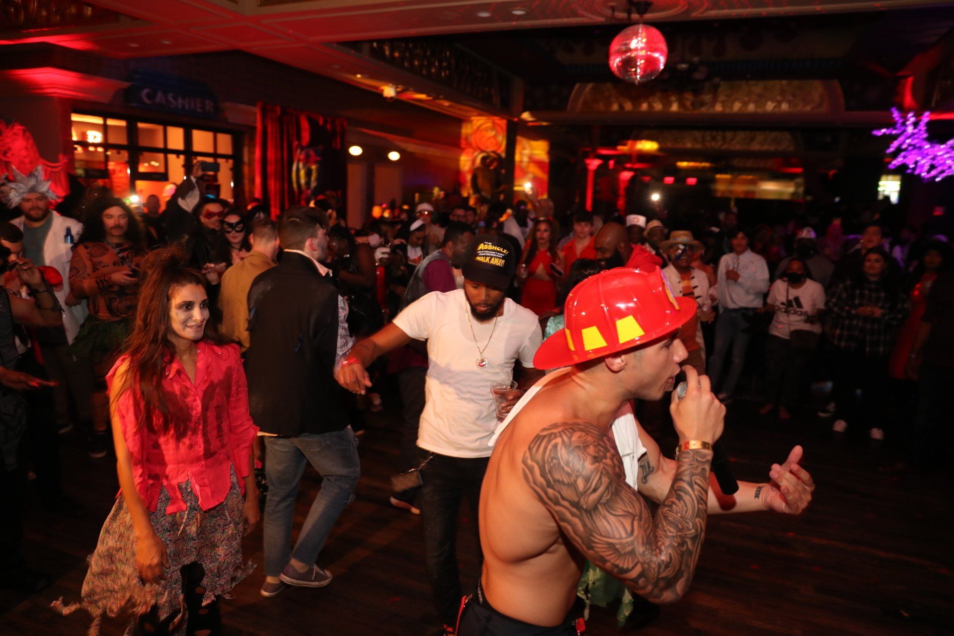A man in a fireman 's hat is singing into a microphone at a party