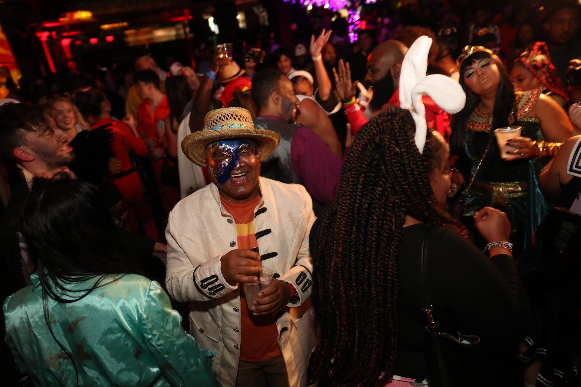 A man in a straw hat is dancing in a crowd of people at a party.