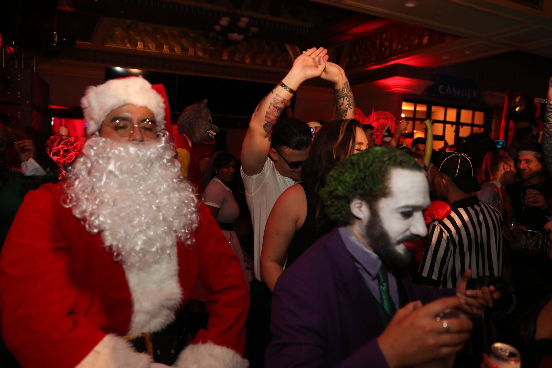 A man dressed as santa claus and a man dressed as the joker are dancing at a party.