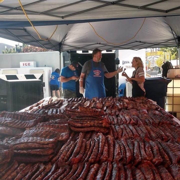 A man in a blue apron is standing in front of a pile of sausages