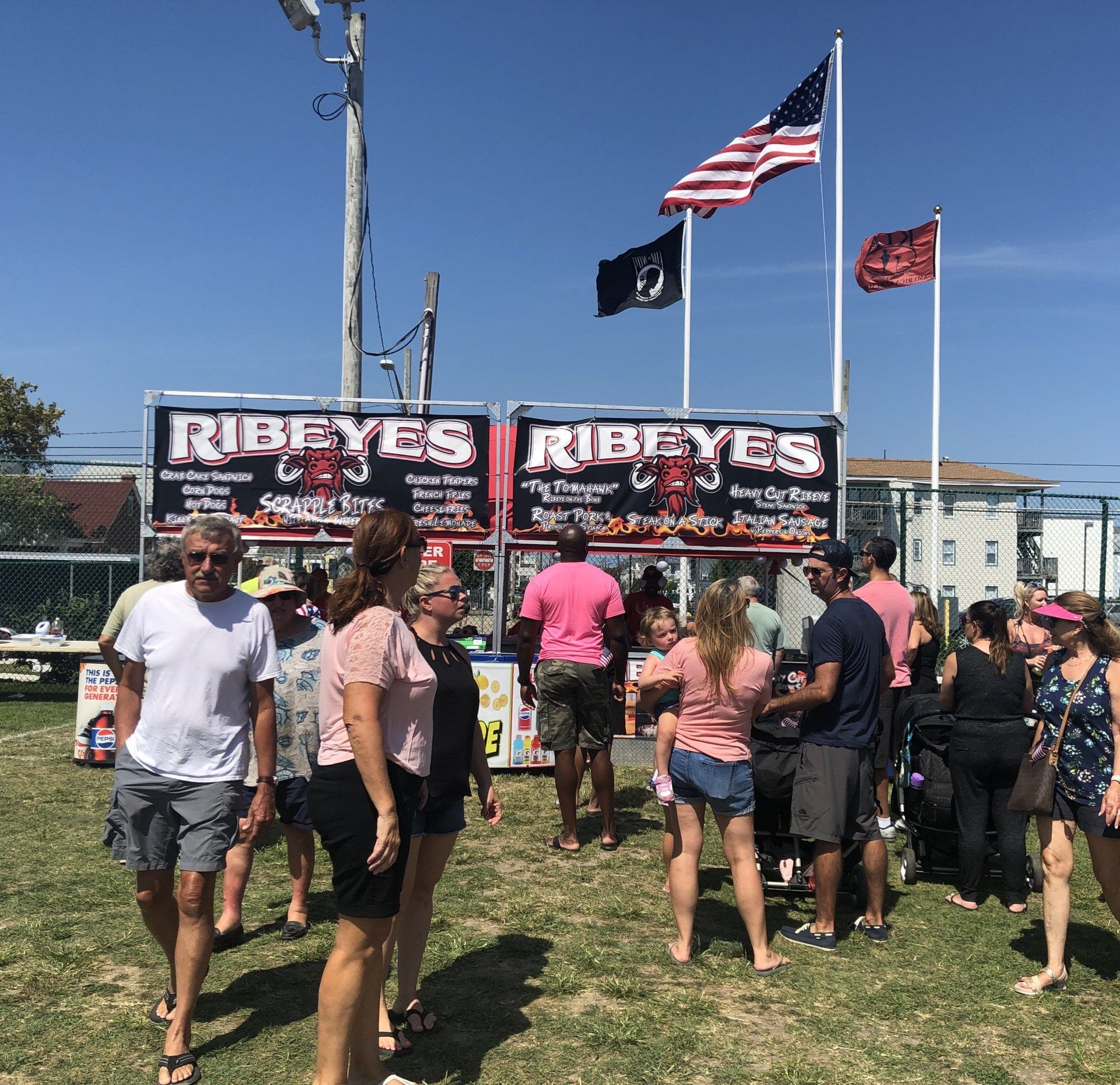 A group of people are standing in front of a food stand called ribeyes