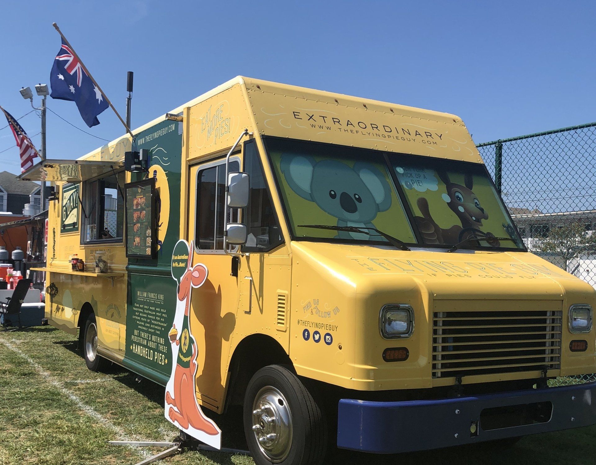 A yellow and green food truck with a koala on the front is parked in a field.