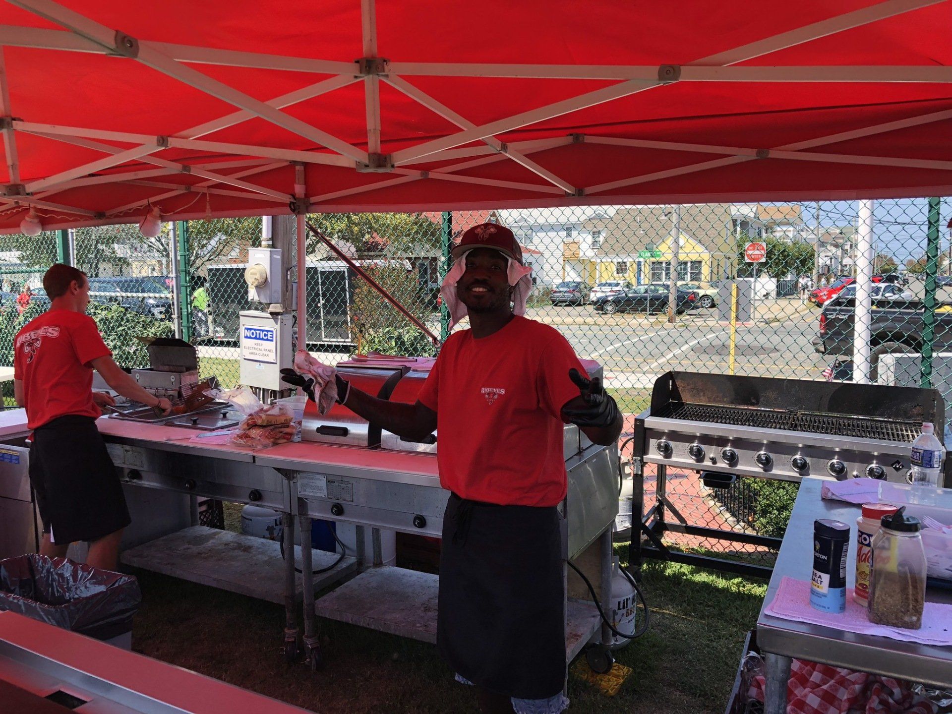 A man in a red shirt is standing in front of a red tent.