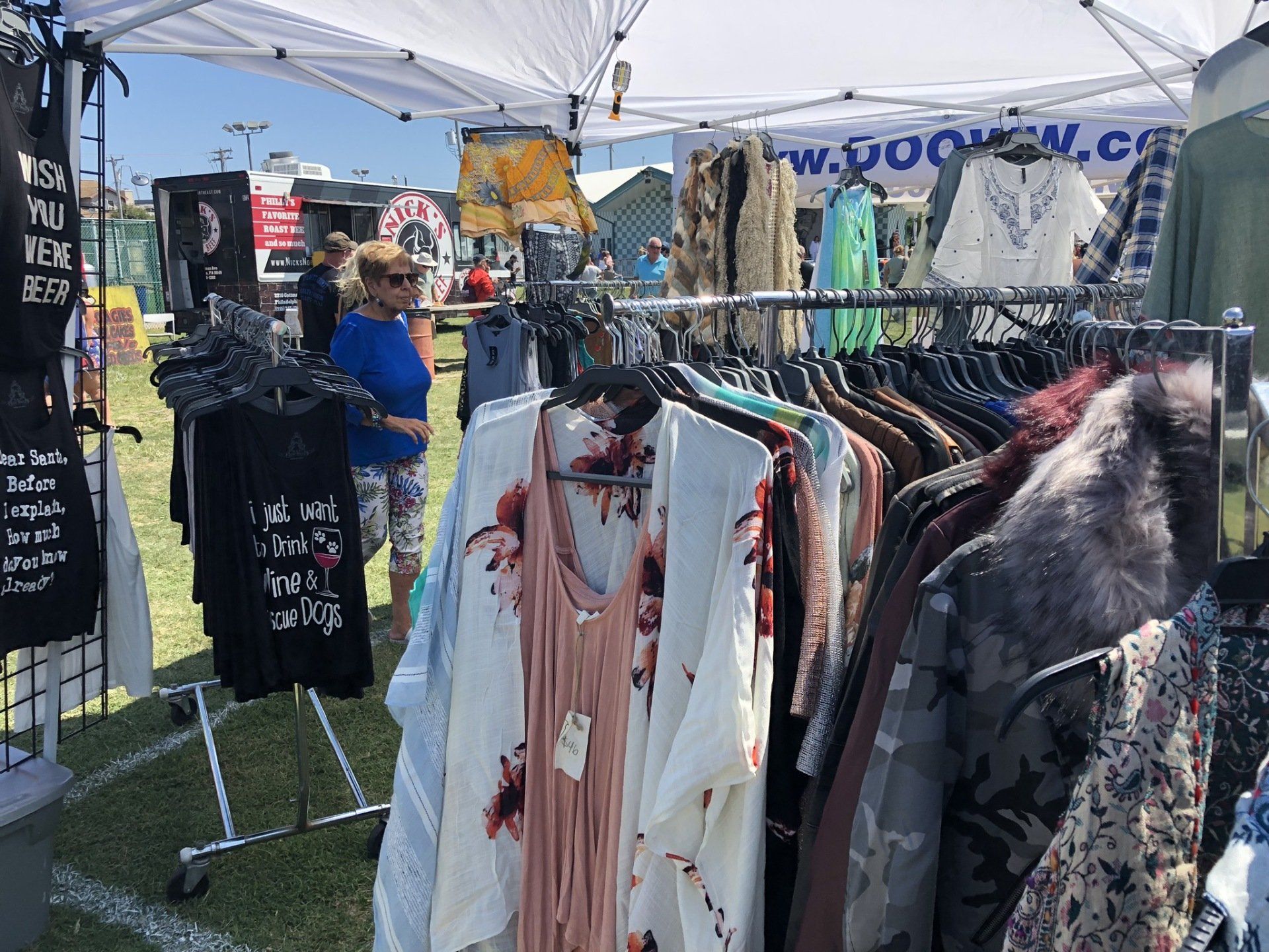 A woman is standing in front of a clothes rack at a market.