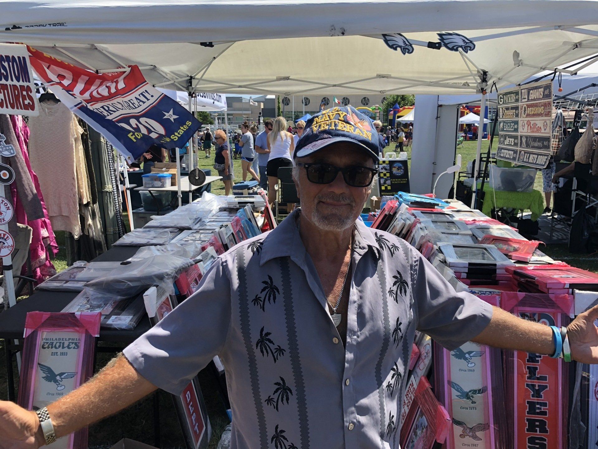 A man is standing in front of a tent at a market.