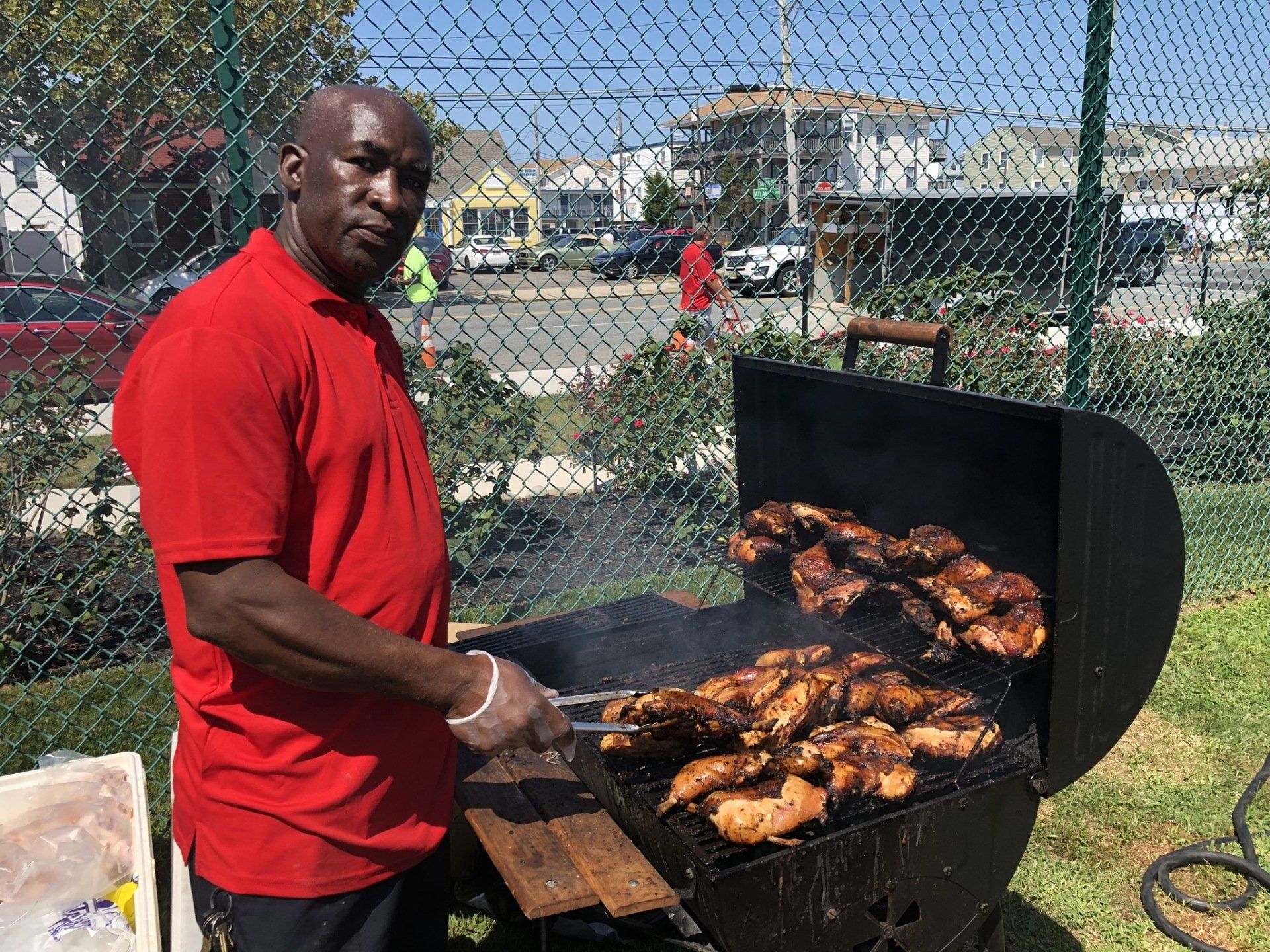 A man in a red shirt is cooking chicken on a grill.