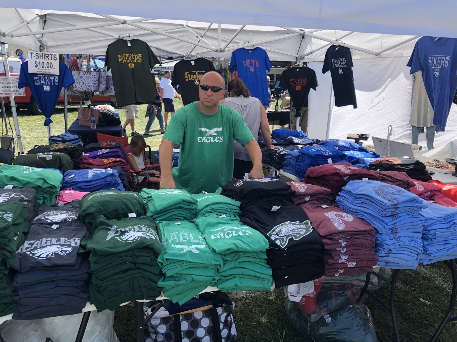 A man in a green shirt is standing in front of a table full of t-shirts.