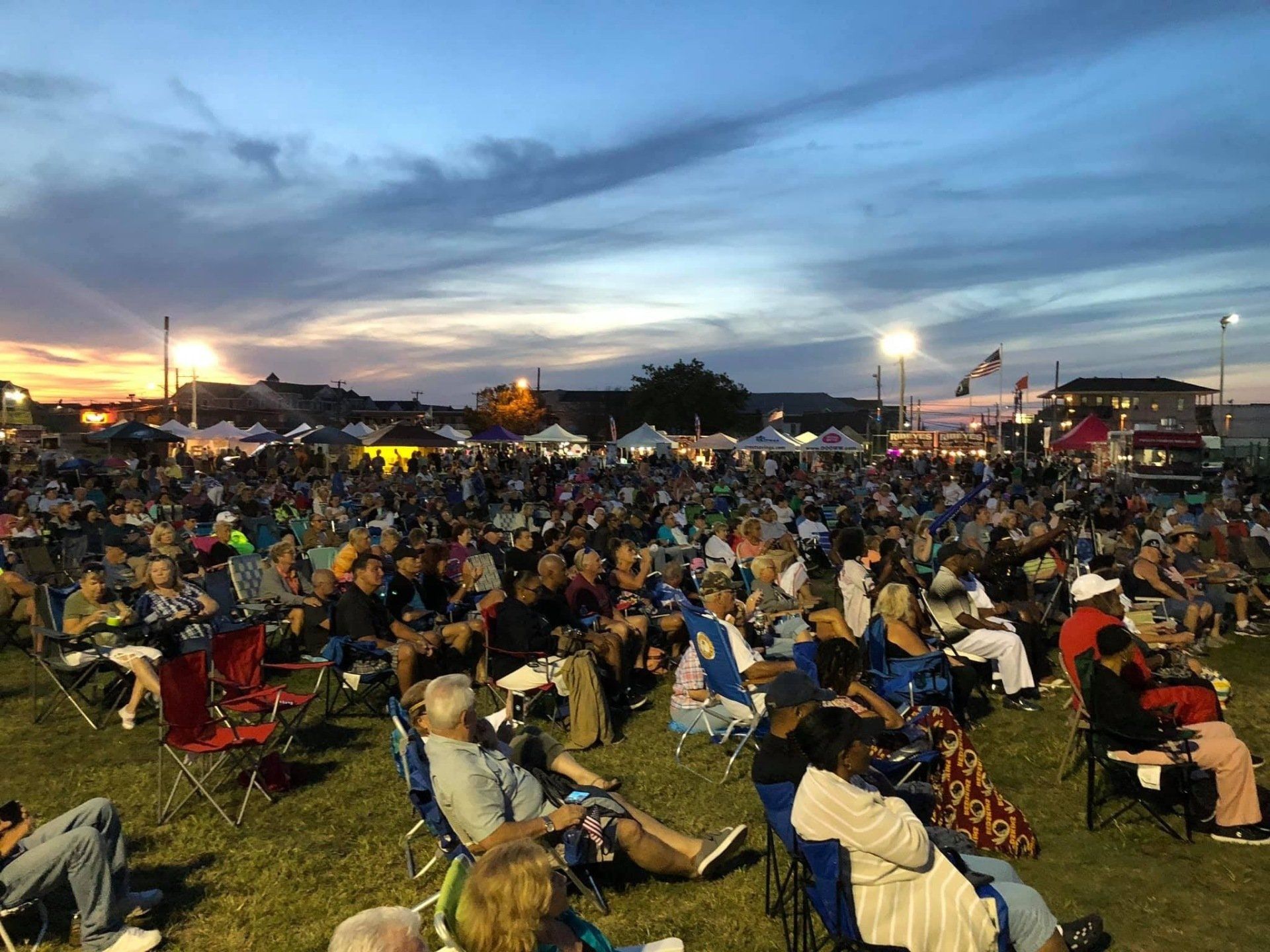 A large group of people are sitting in chairs in a field at a concert.