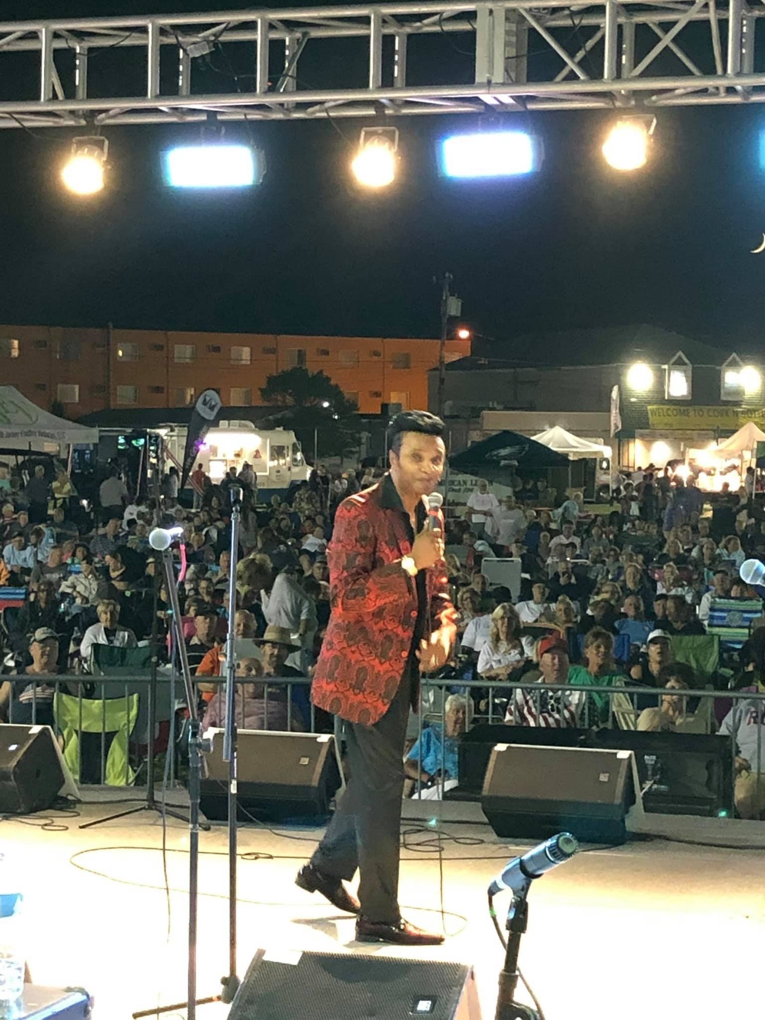 A man in a red jacket is standing on a stage holding a microphone.