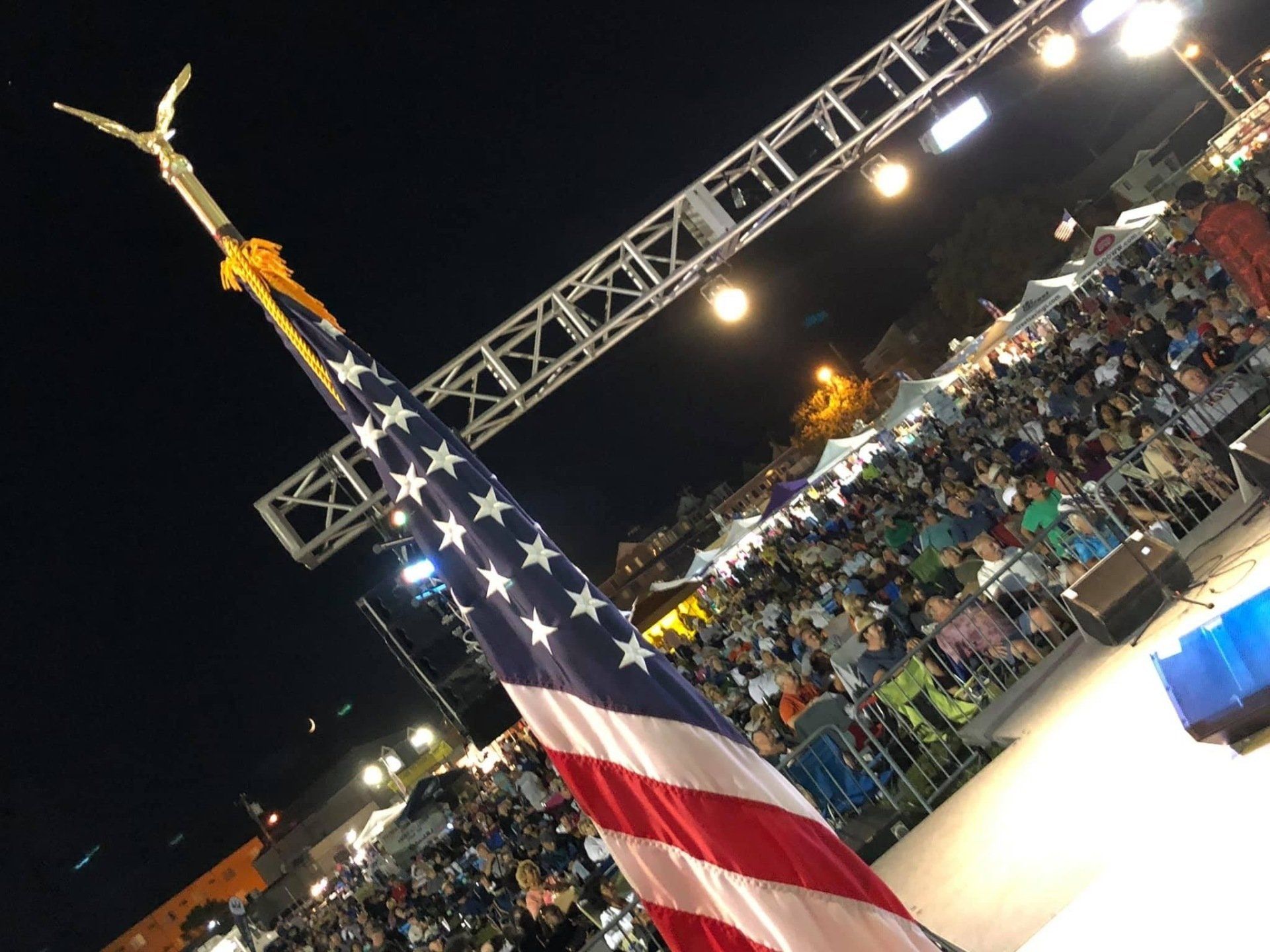 A crowd of people are gathered in front of an american flag