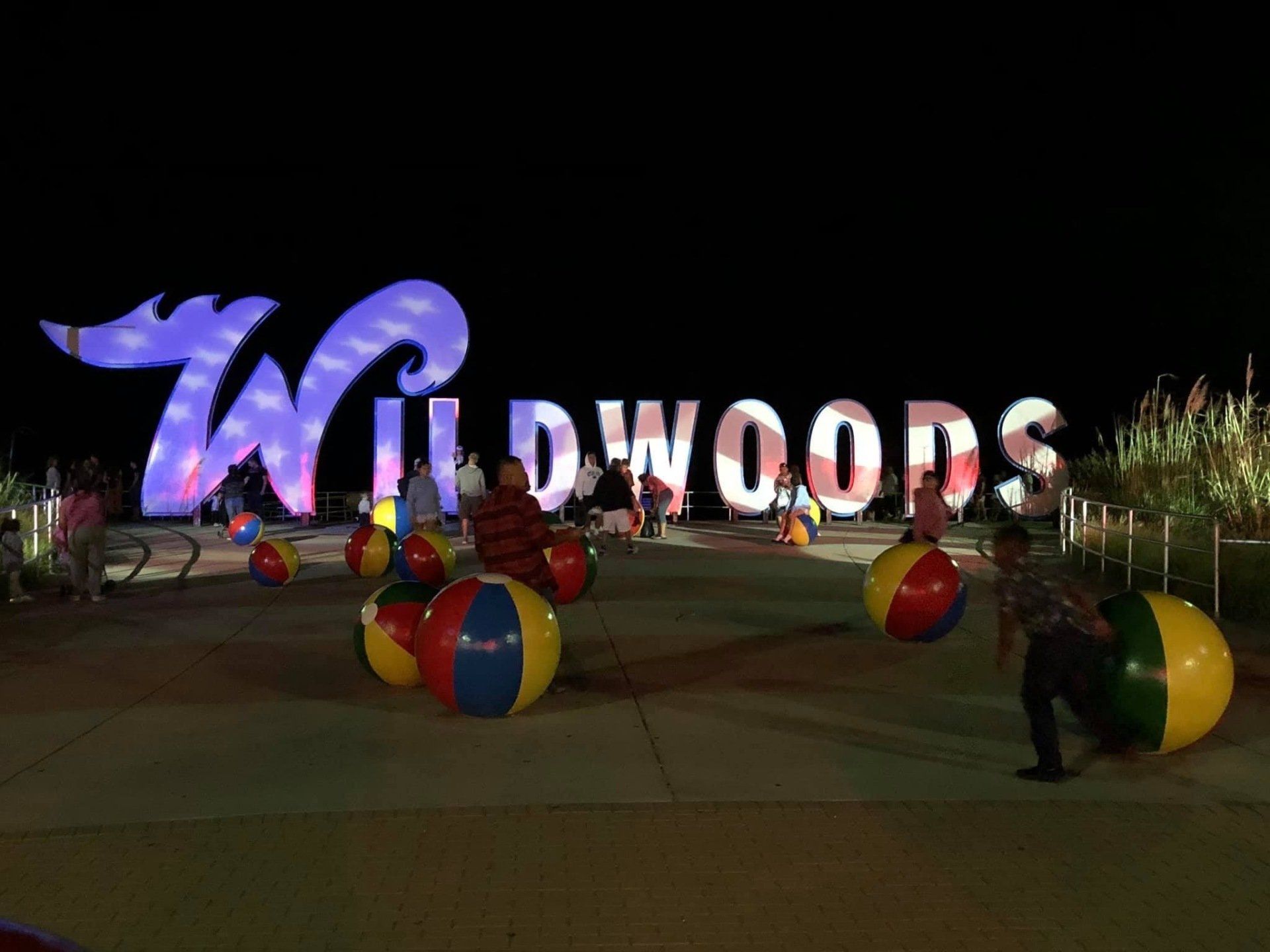 A group of people are playing with beach balls in front of a sign that says wildwoods.
