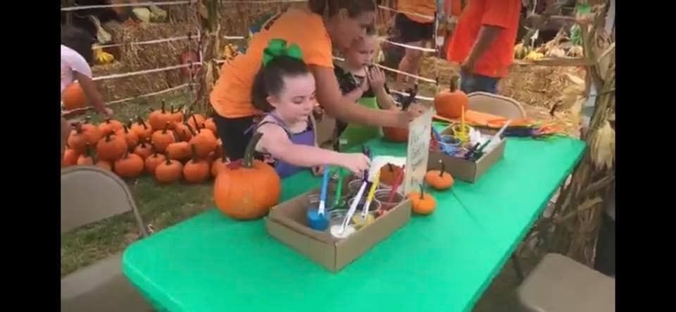 A little girl is sitting at a table at a pumpkin patch.