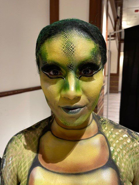 A woman with green face paint is wearing a turtle costume.