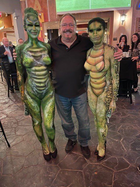 A man is standing next to two women in body paint.
