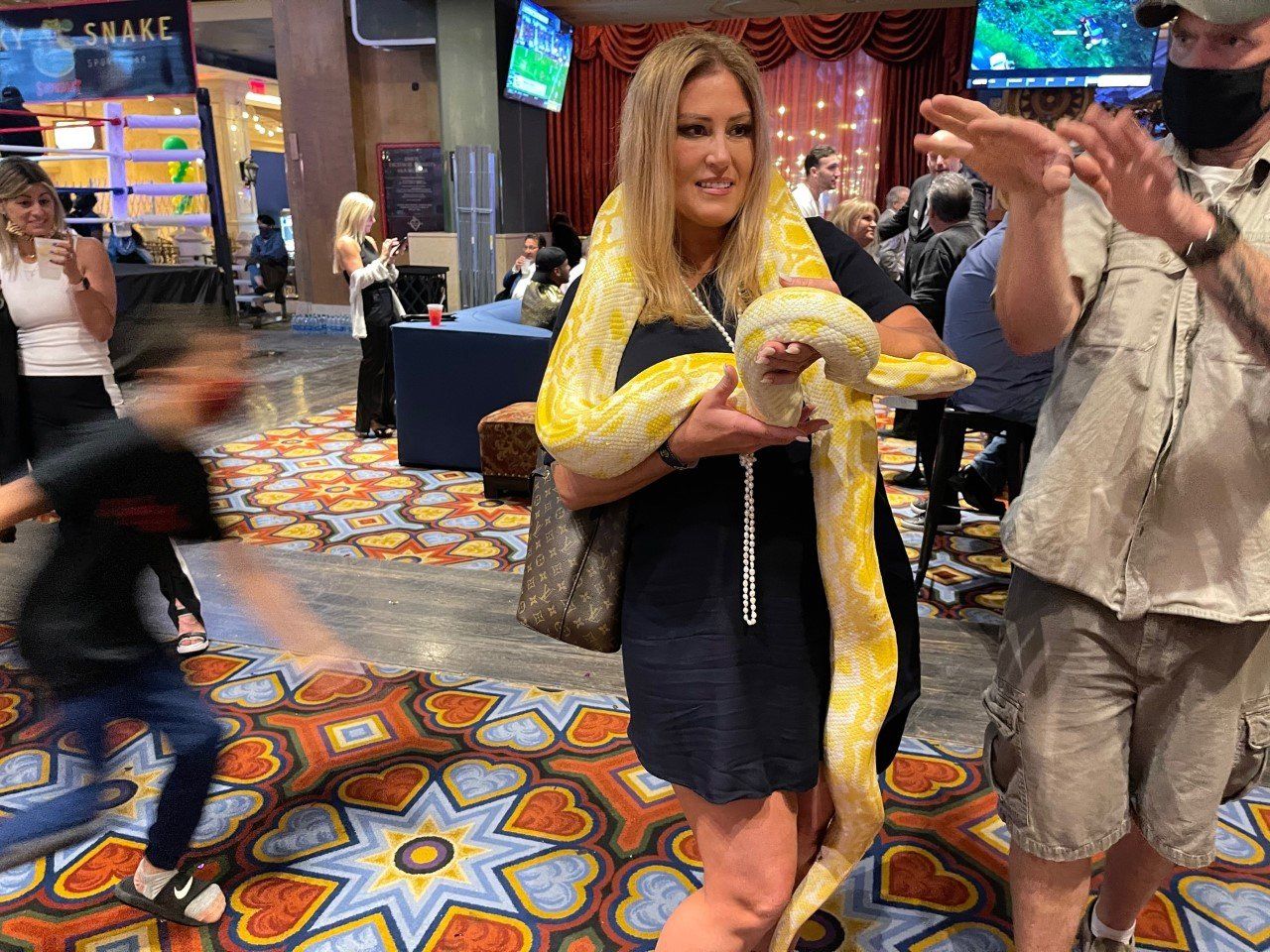 A woman is holding a large yellow snake in her hands.