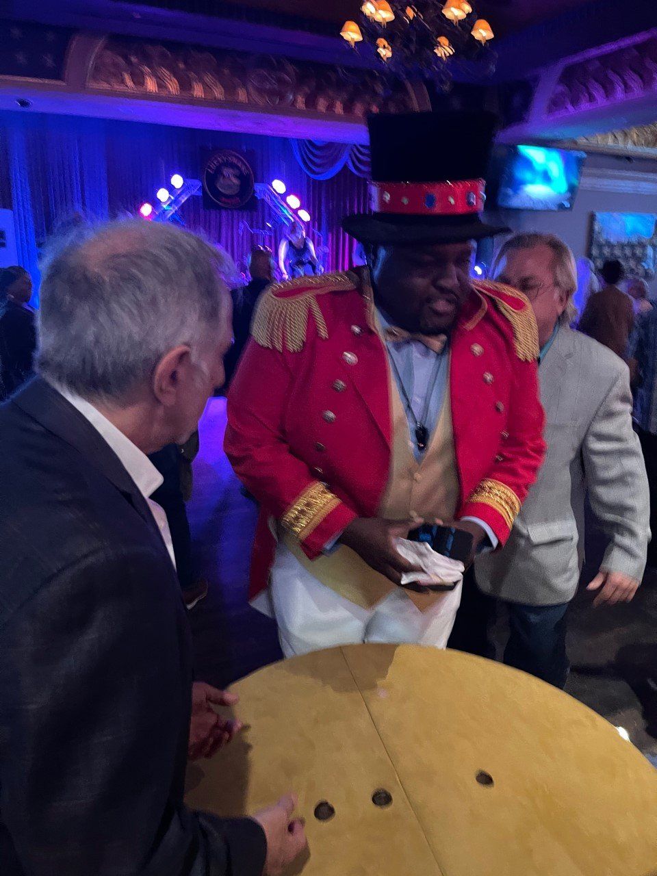 A man in a red jacket and top hat is talking to a man in a suit.