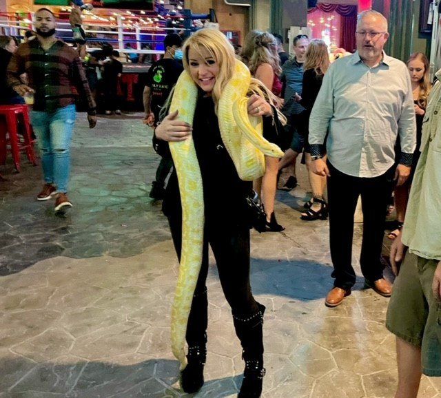 A woman is holding a large yellow snake around her neck.