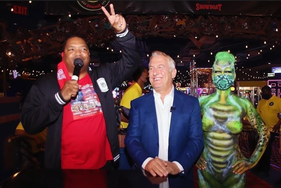 A man with a microphone stands next to a woman with body paint