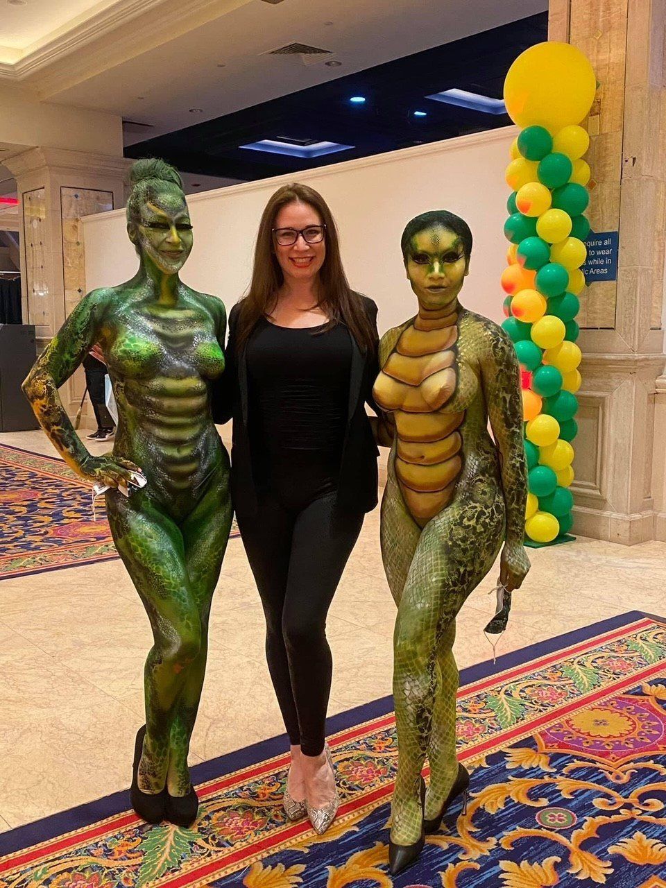 A woman is standing next to two women in body paint.