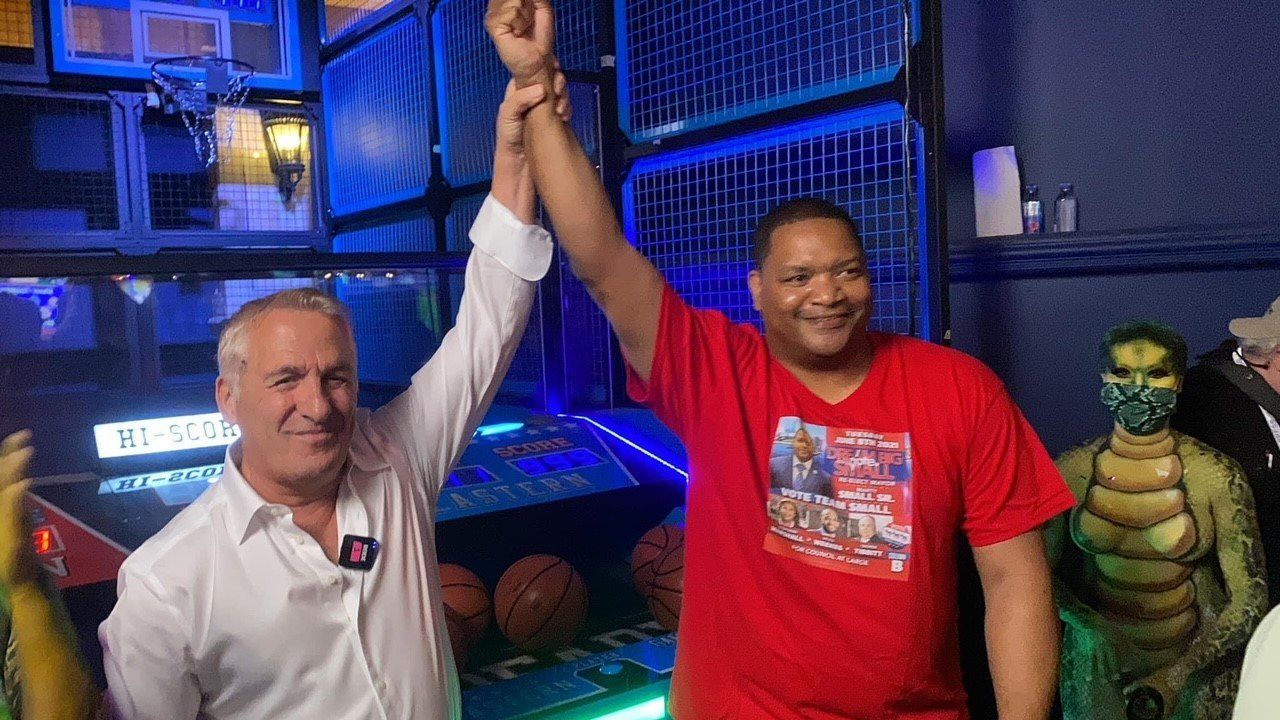 Two men are standing next to each other with their arms in the air.