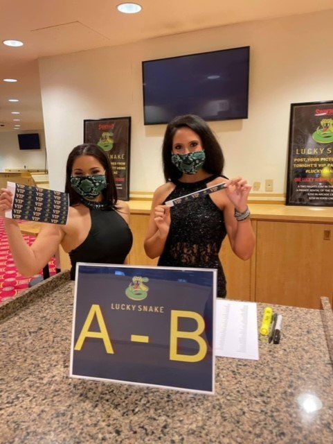 Two women wearing masks are standing in front of a sign that says a-b