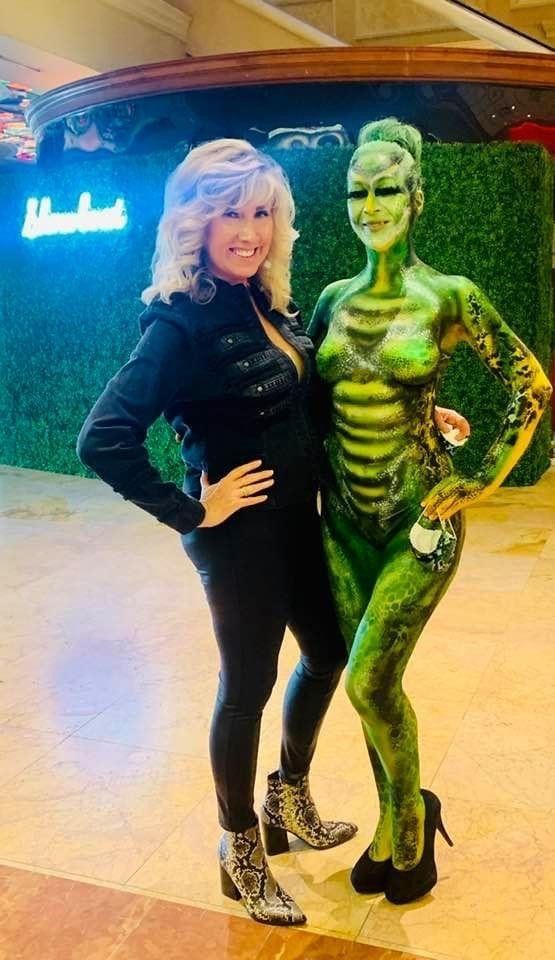 A woman is standing next to a woman with her body painted green.