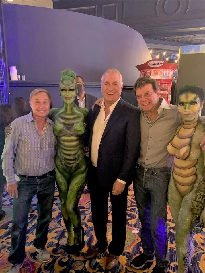 A group of men are posing for a picture with a woman in a green body paint costume.