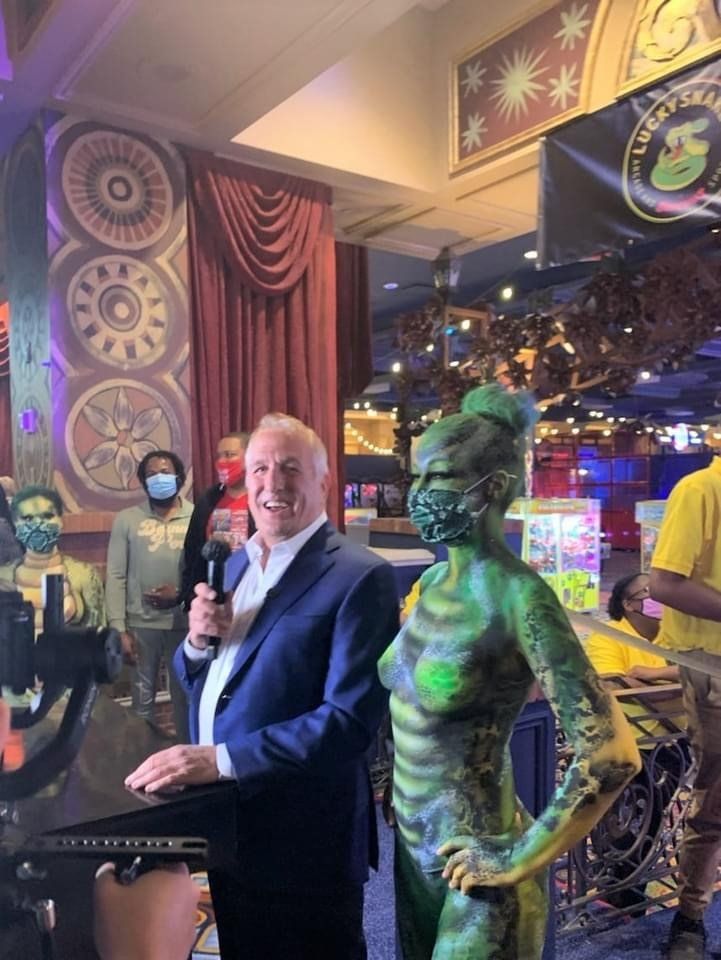 A man in a suit is standing next to a woman with green paint on her body.