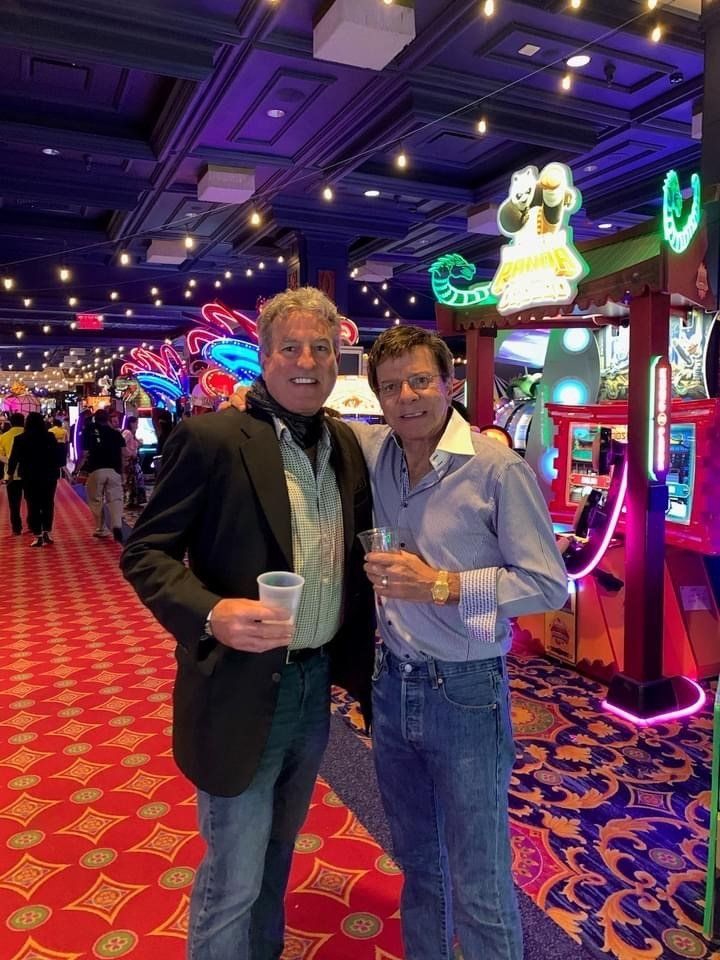 Two men are standing next to each other in a casino holding drinks.