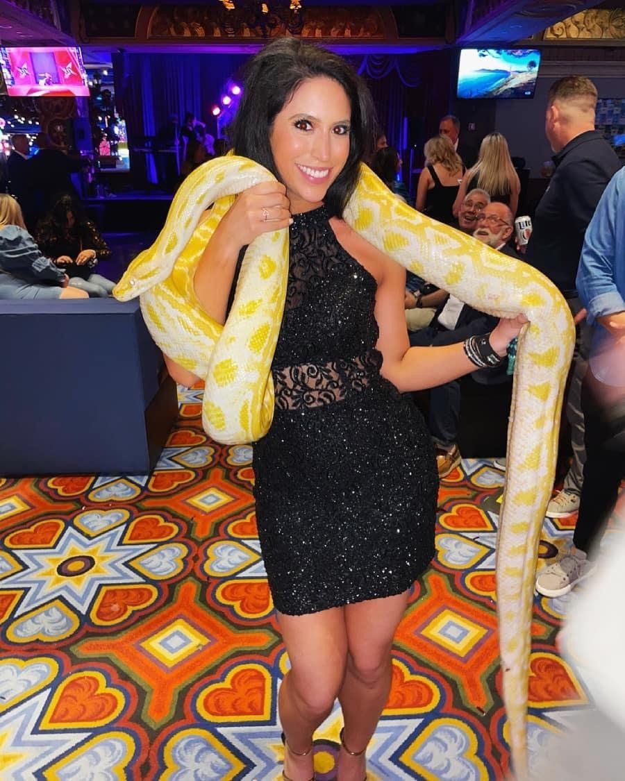 A woman in a black dress is holding a large yellow snake.