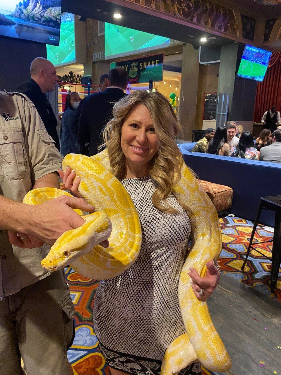 A woman is holding a large yellow snake in her hands.
