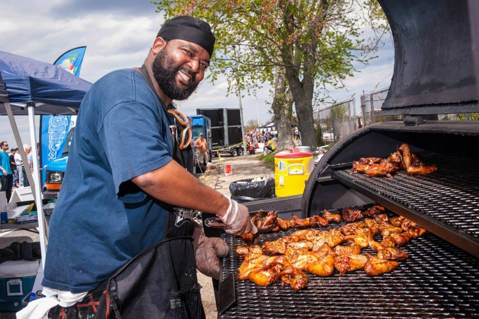 A man is cooking chicken wings on a grill.
