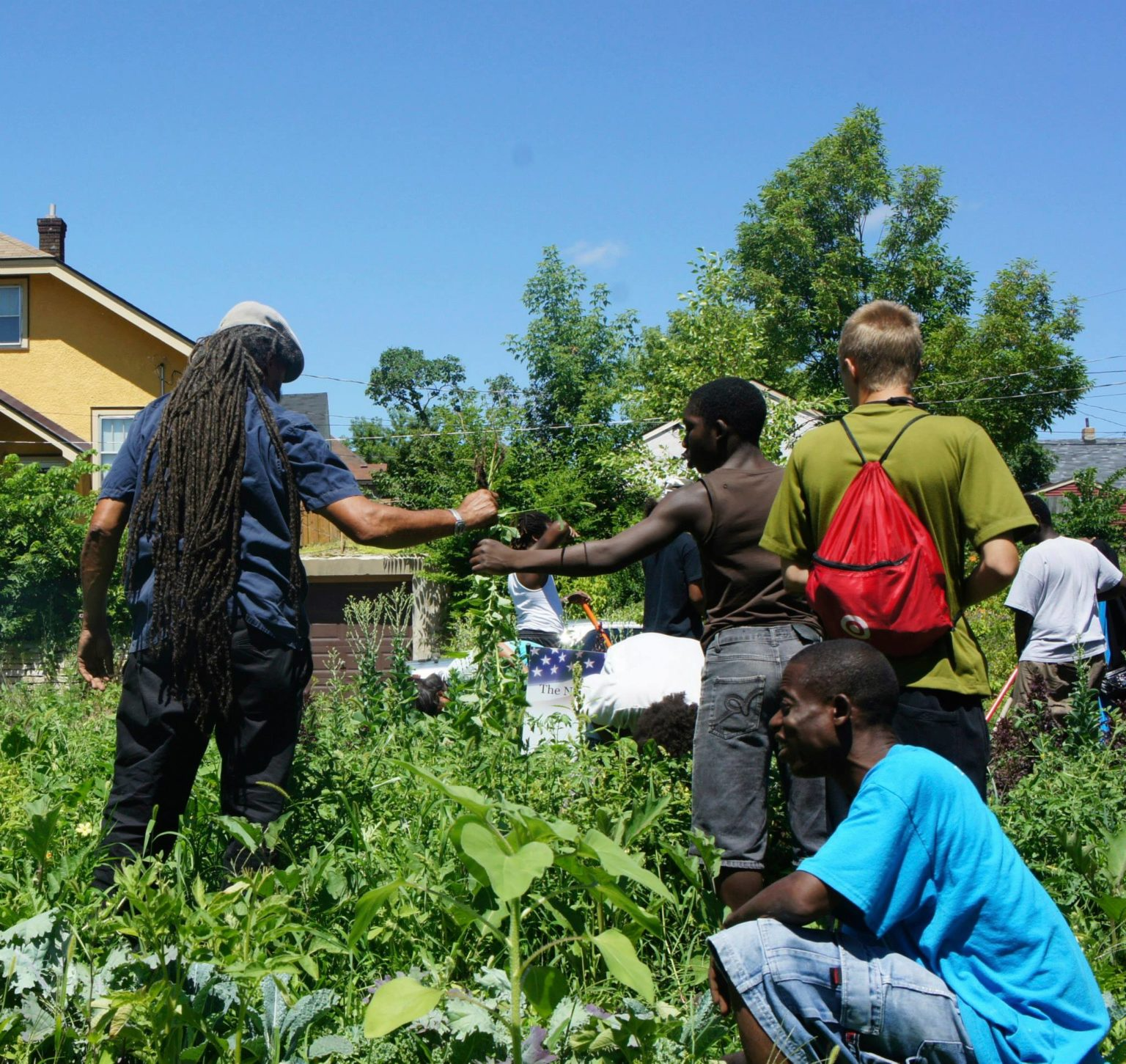 A group of people standing in a field with a yellow house in the background