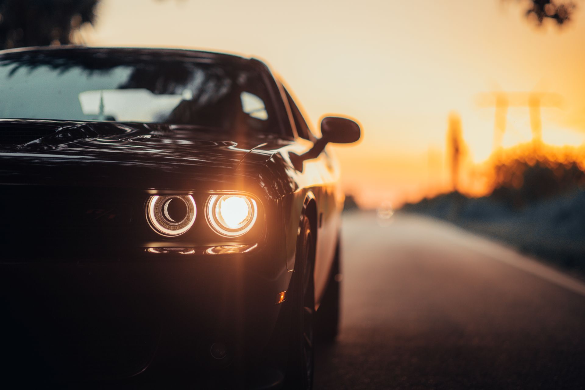 A close up of a car 's headlights on a road at sunset.