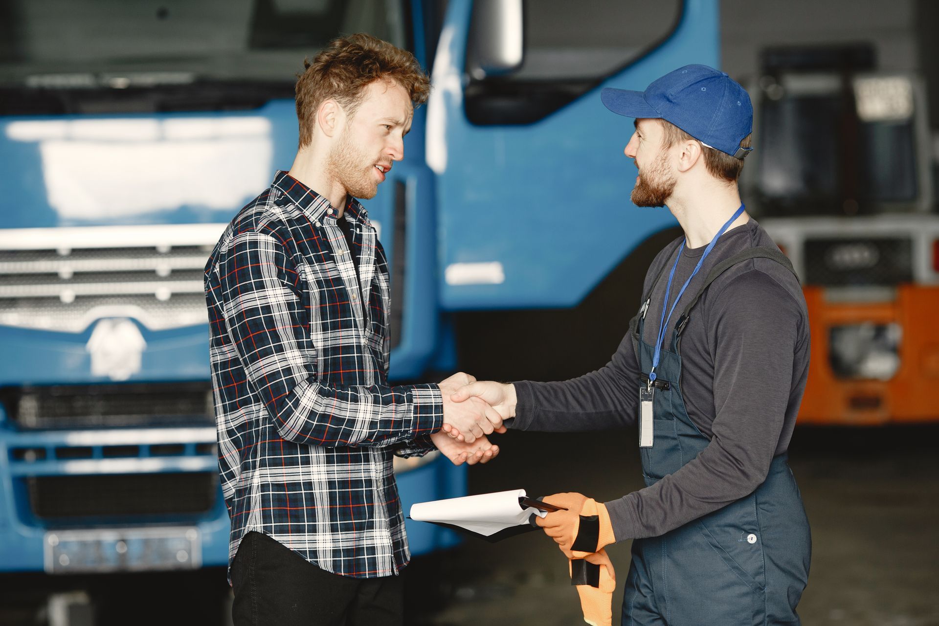 Two men are shaking hands in front of a truck in a garage.