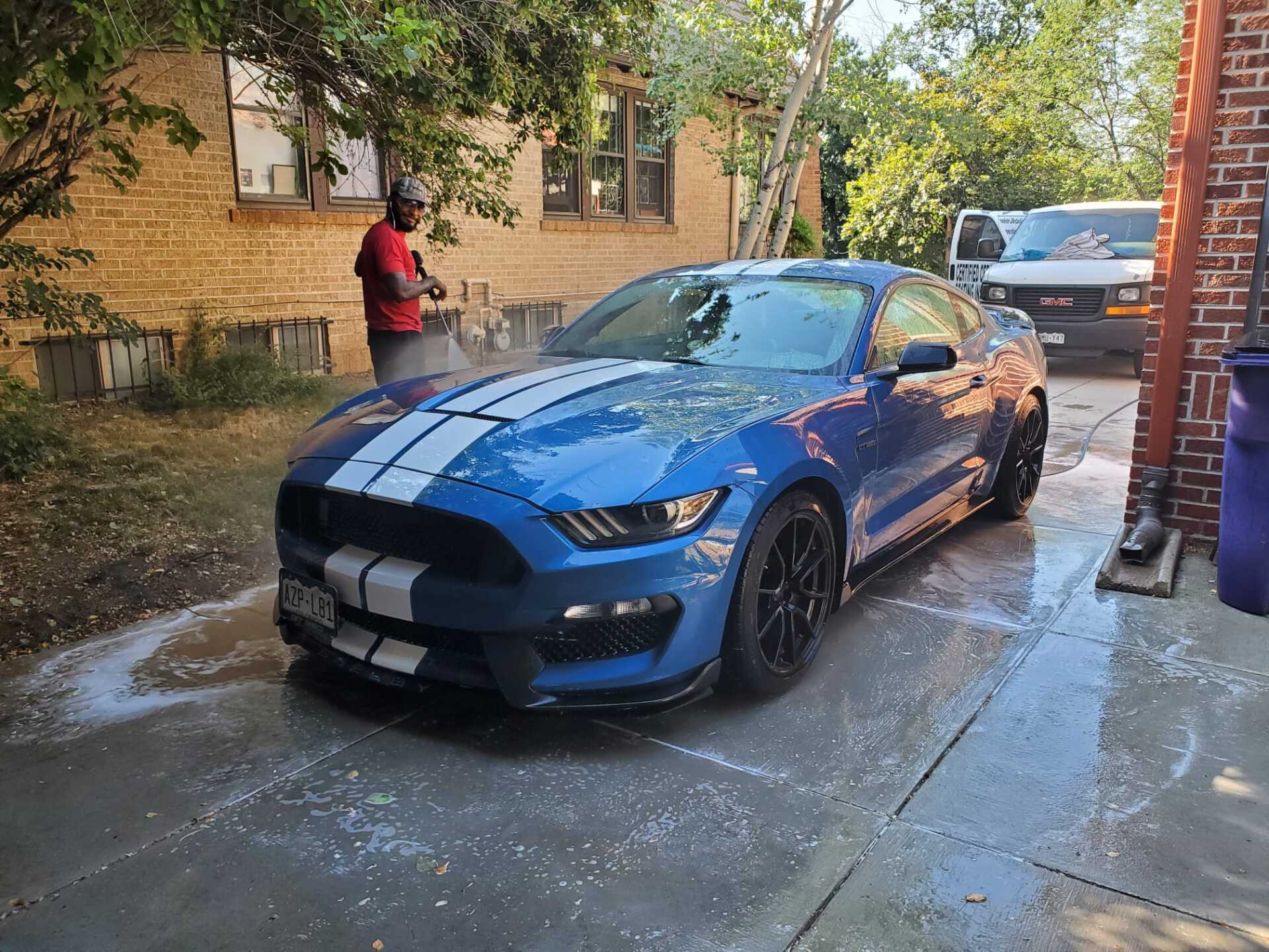 a man is washing a blue mustang in a driveway .