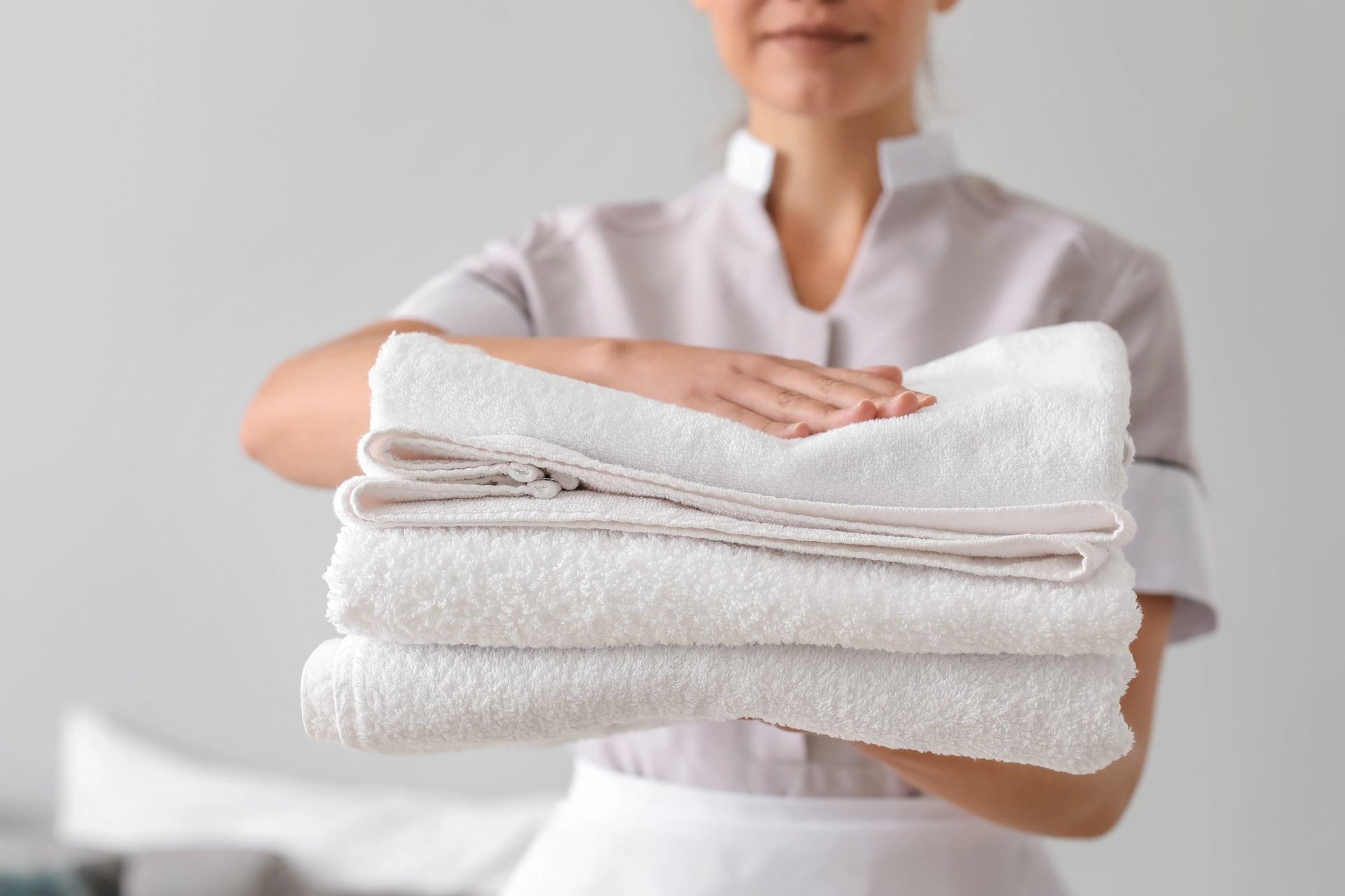 Persona in uniforme che tiene in mano una pila di asciugamani bianchi piegati con cura.